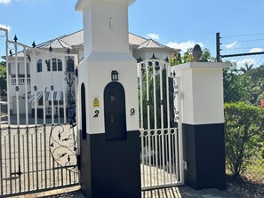 A gated entrance with a CCTV warning sign, numbered gates, and a building with a tiled roof in the background.