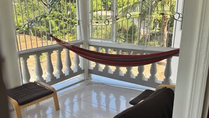 A balcony with a hammock, two chairs, and a view of greenery.