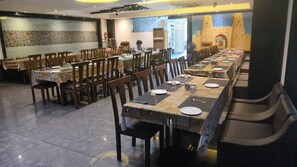 A restaurant with multiple tables and chairs, a tiled floor, and a mural on the wall. - JMC HOTEL SOTEL INDORE (Indore)