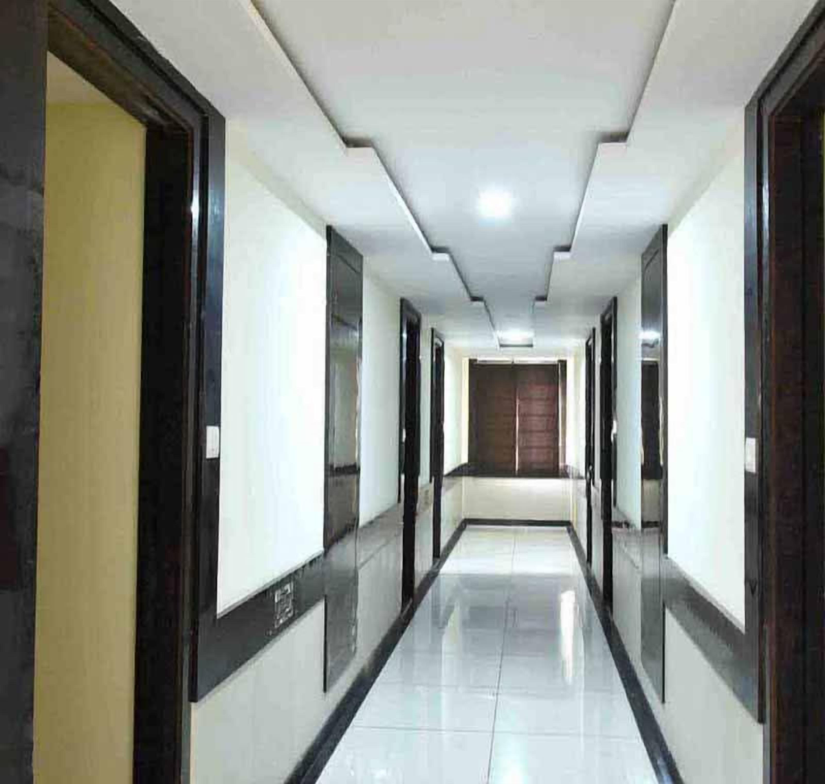 A long, narrow hallway with doors on both sides, leading to rooms. The floor is tiled, and the walls are white with dark trim.