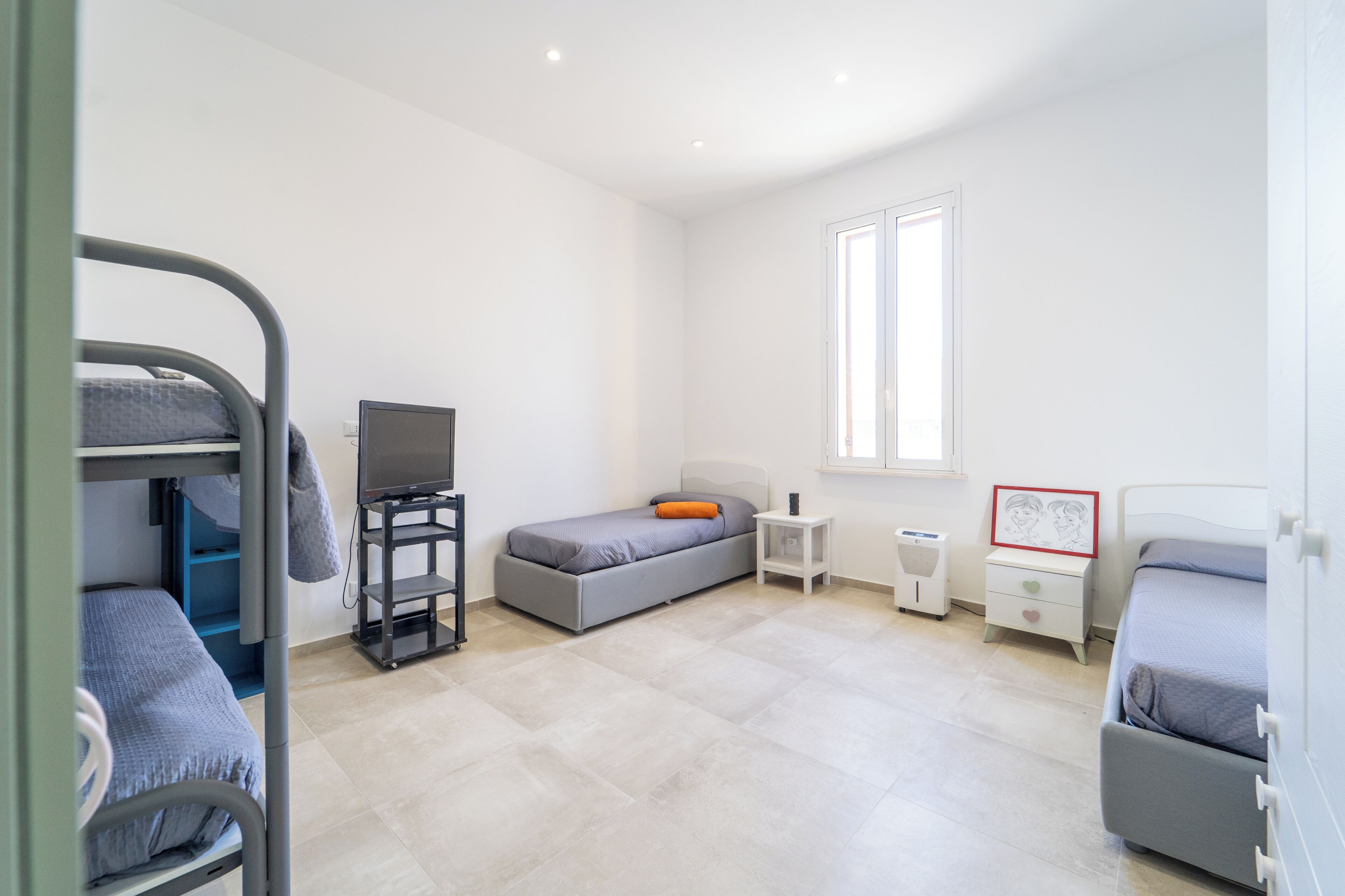 A bedroom with bunk beds, a desk, a chair, a TV, a bedside table, a window, and a framed picture.