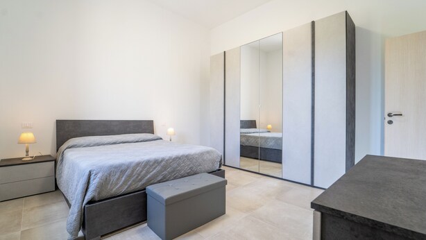 Ein modernes Schlafzimmer mit Bett, Nachttischen, einer Bank, einem Kleiderschrank und einem Spiegel.