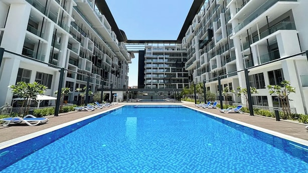 A modern hotel with a central swimming pool, multiple balconies, and a clear sky. - Bloomfields 1BR in Oasis Masdar  (Abu Dhabi)