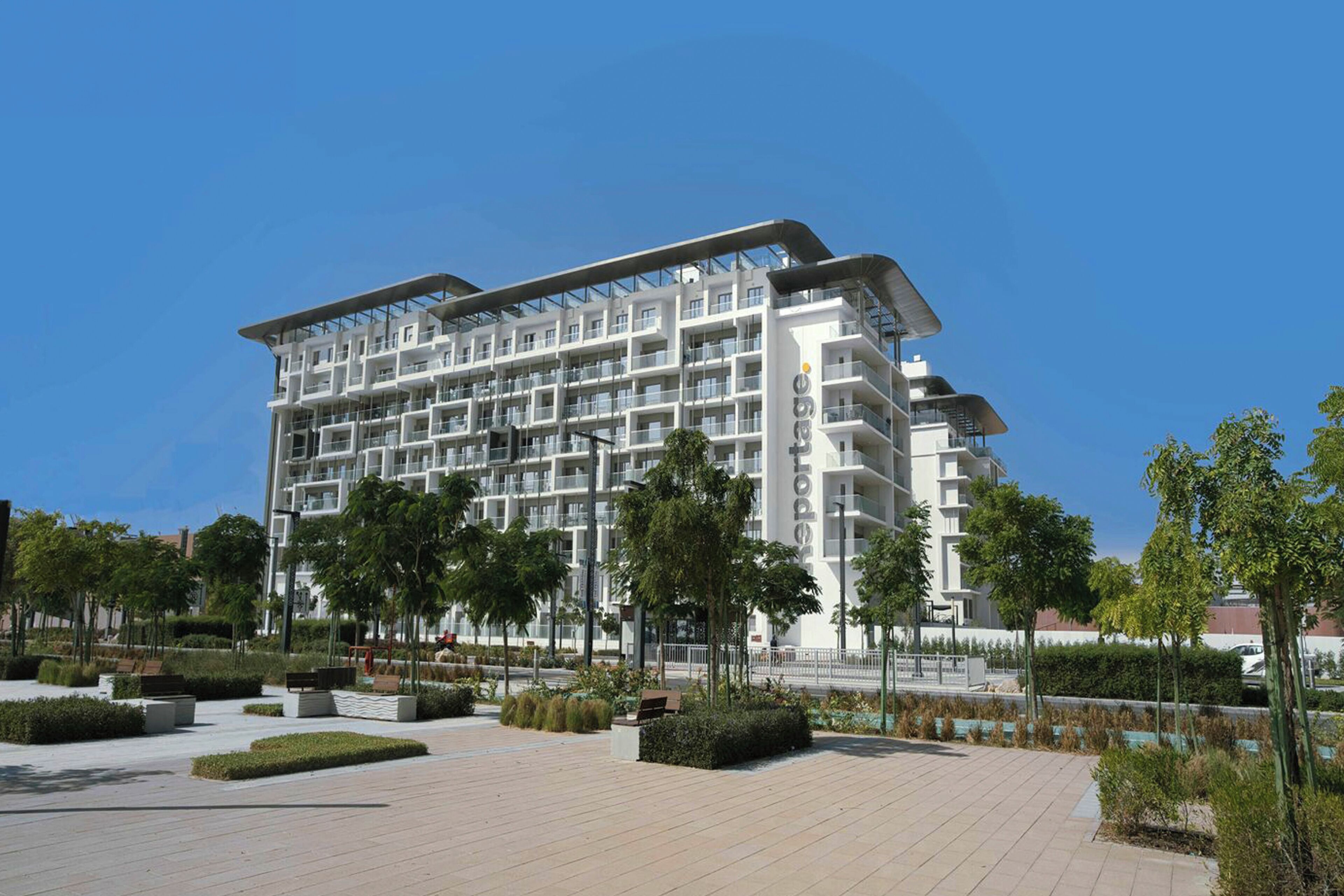 A multi-story hotel with balconies, a landscaped courtyard, and a clear sky.