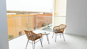 A balcony with two wicker chairs and a small table, overlooking a building with wooden panels. - Bloomfields 1BR in Oasis Masdar  (Abu Dhabi)