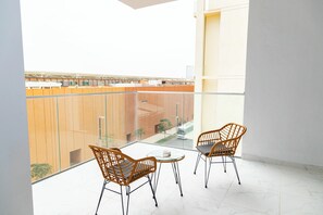 A balcony with two wicker chairs and a small table, overlooking a building with wooden panels. - Bloomfields 1BR in Oasis Masdar  (Abu Dhabi)