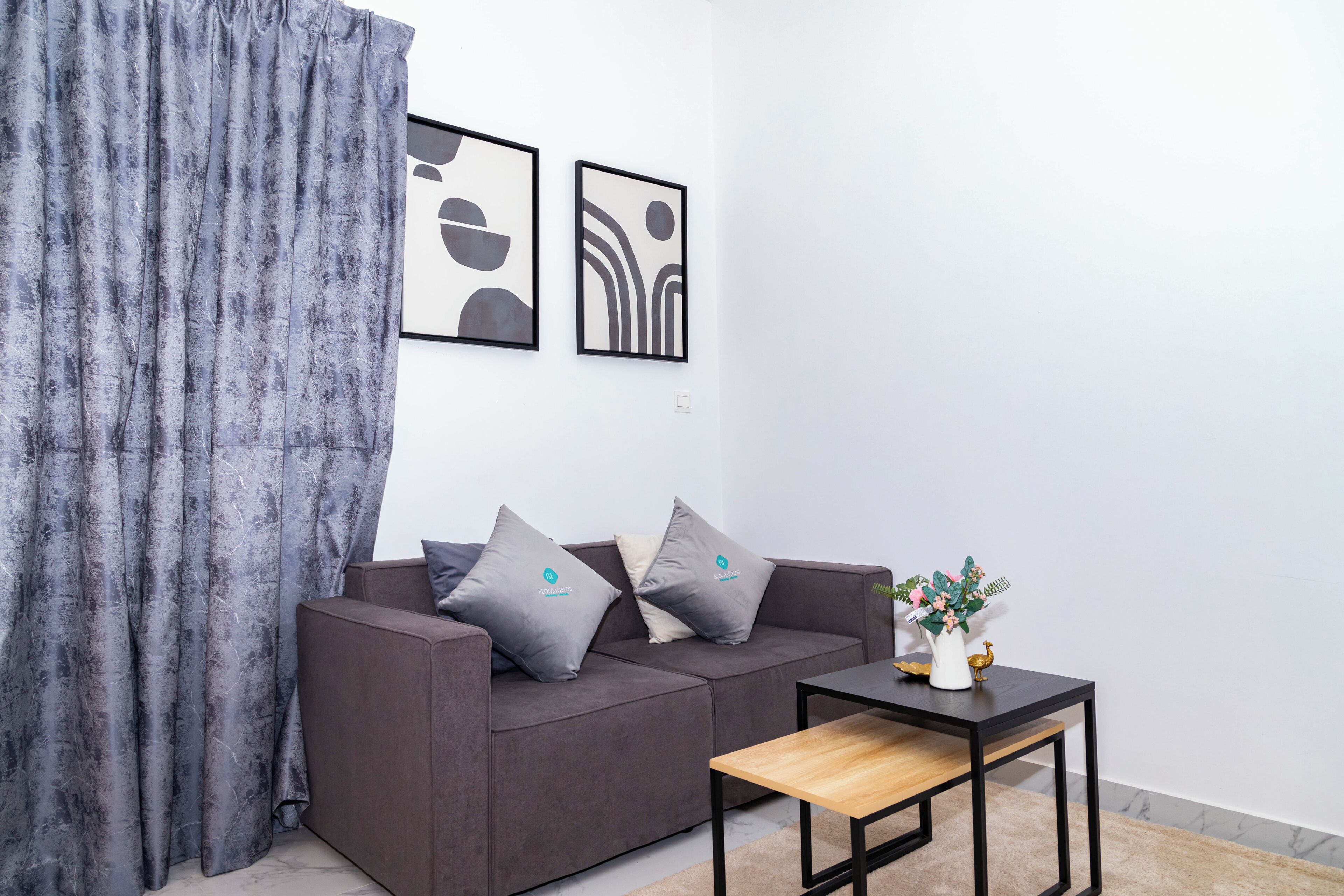 Ein modernes Wohnzimmer mit einem grauen Sofa, zwei Kissen, einem kleinen Holztisch und abstrakter Wandkunst.
