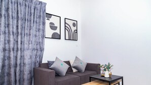 A modern living room with a grey sofa, two cushions, a small wooden table, and abstract wall art. - Bloomfields 1BR in Oasis Masdar  (Abu Dhabi)