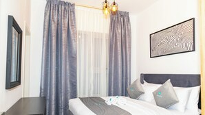 A neatly made bed with pillows and a blanket, a bedside table, a framed picture on the wall, and a window with curtains. - Bloomfields 1BR in Oasis Masdar  (Abu Dhabi)