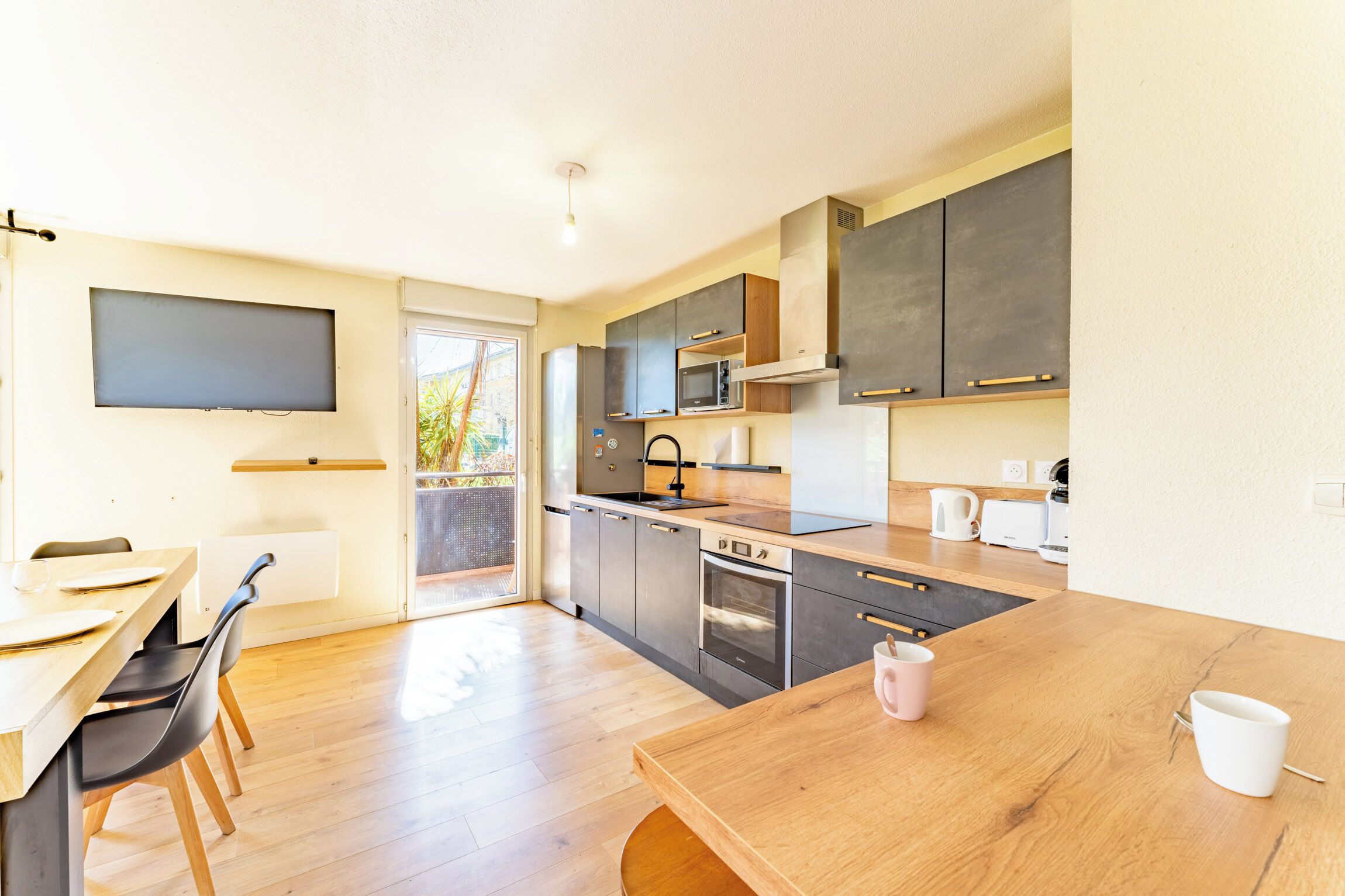 Una cocina moderna con una mesa de comedor de madera, electrodomésticos integrados y un ventanal corredero a un balcón.