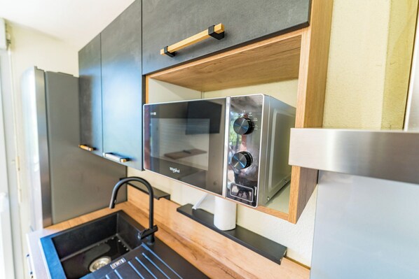 A compact kitchen with a microwave, stove, and wooden cabinetry.