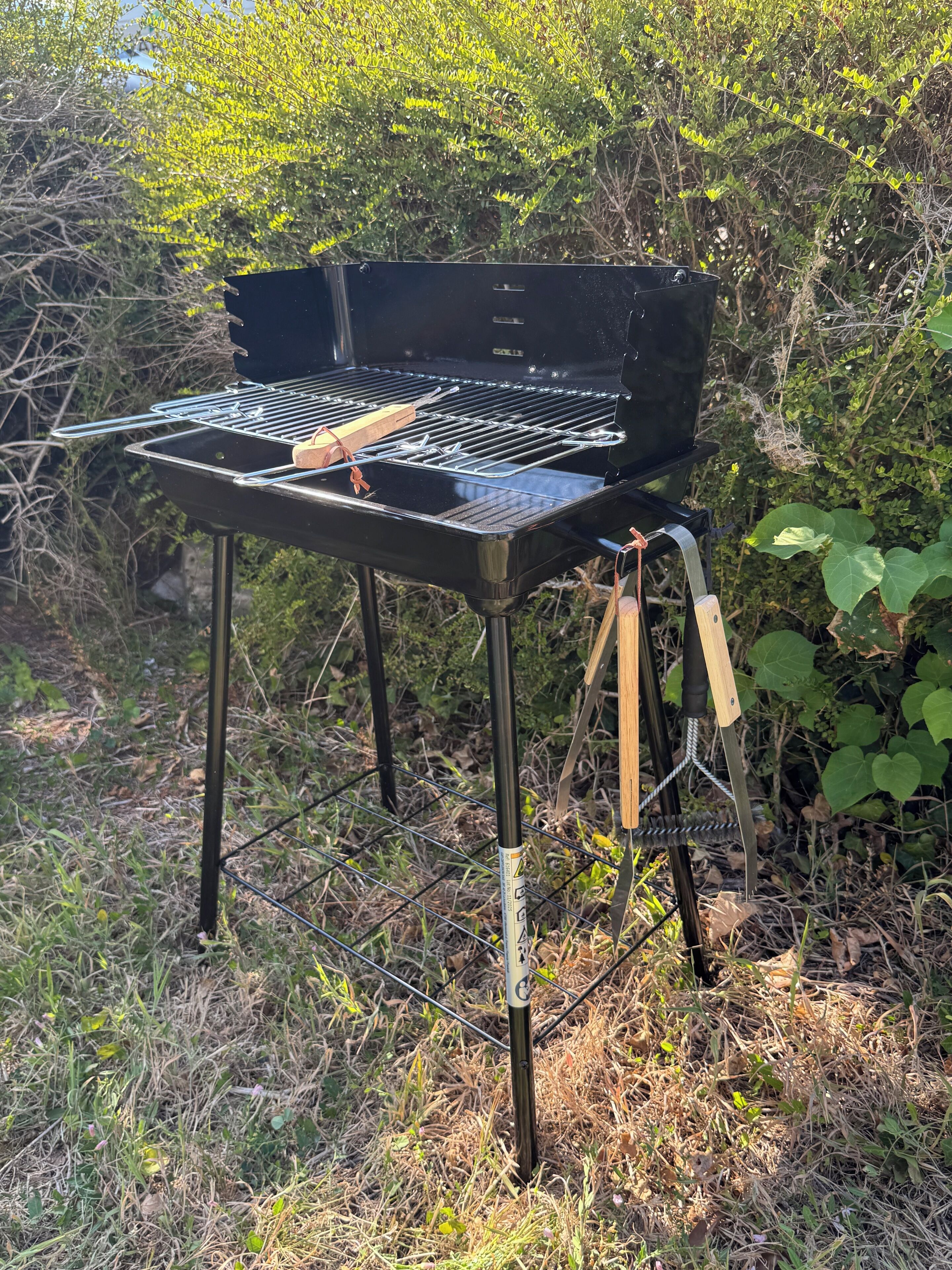 Een draagbare grill buiten opgesteld, met een metalen frame en een zwart kookrooster.