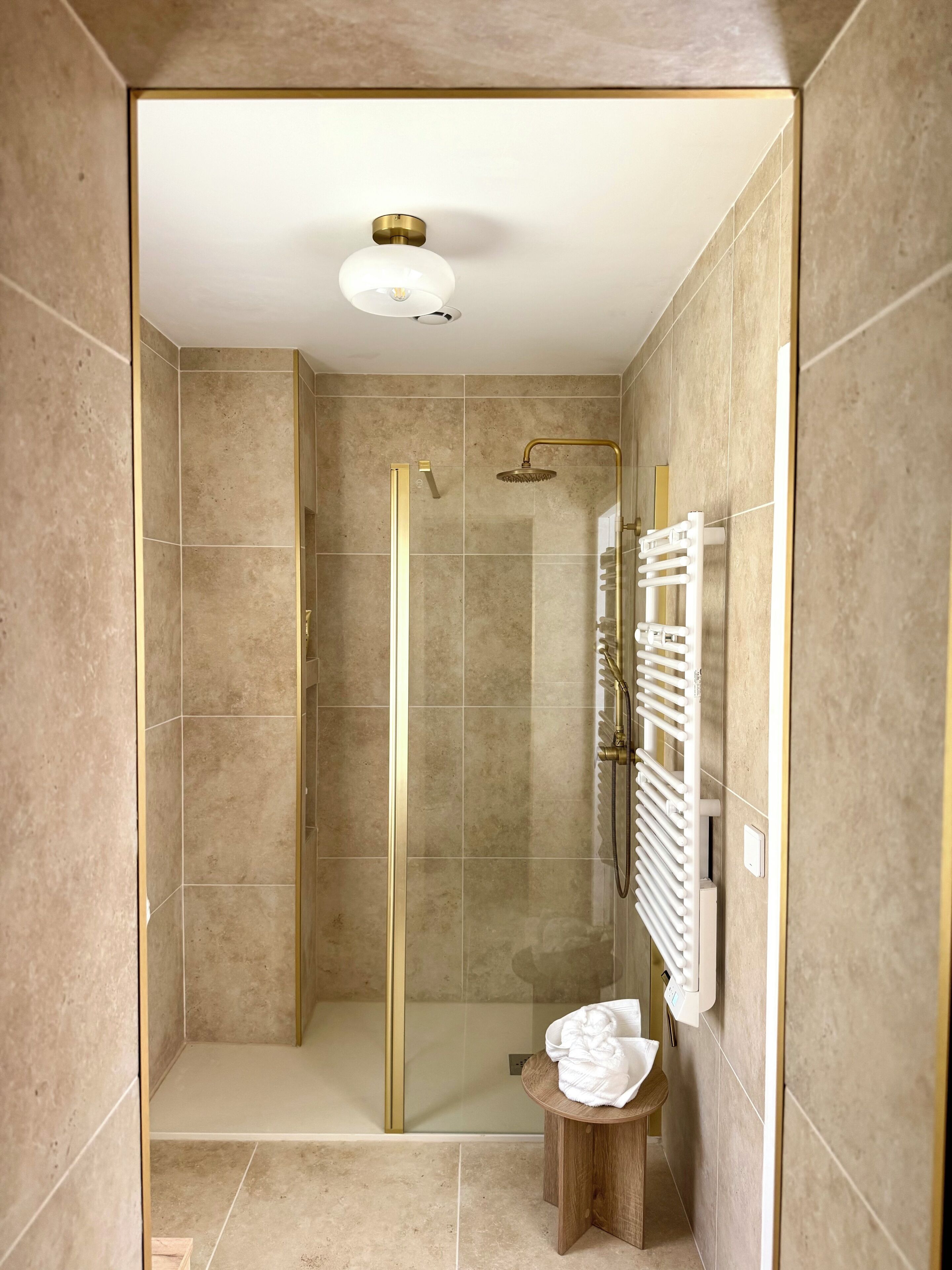 A shower with a glass door, a white towel rack, and a wooden stool.
