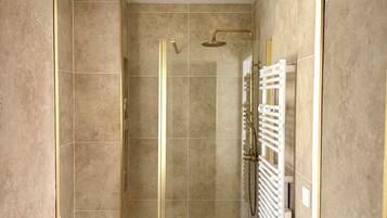 A shower with a glass door, a white towel rack, and a wooden stool.