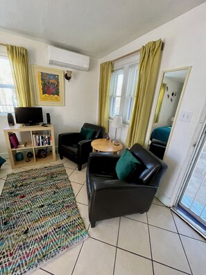 A living room with a sofa, a small table, a bookshelf, a patterned rug, and a window with curtains. - Sunny Garden Hideaway in Historic Tucson Neighborhood (Tucson)