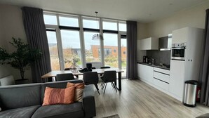 A modern living room with a sofa, dining table, and kitchen area with cabinets and appliances. - Just Nature Miva 6 (Hindeloopen)