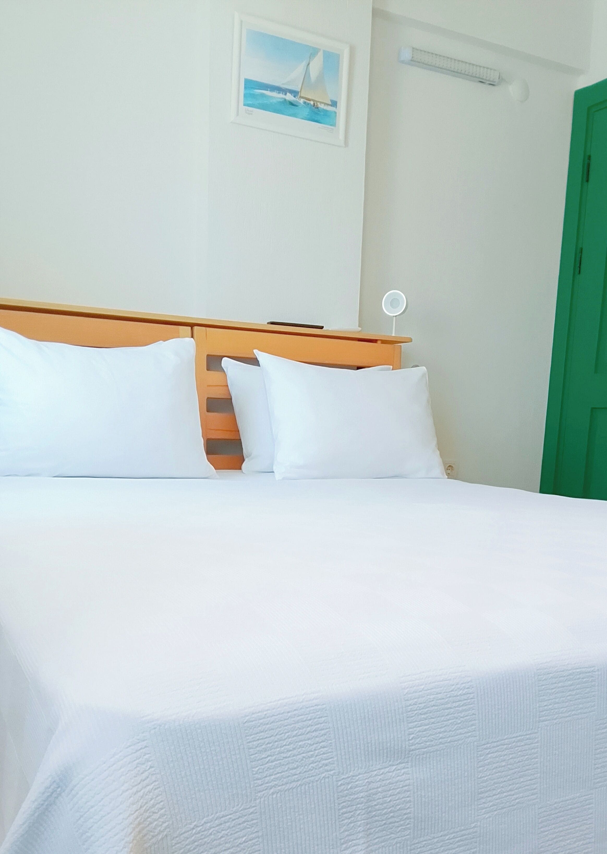 A bed with white linens, a wooden headboard, and a small picture on the wall.