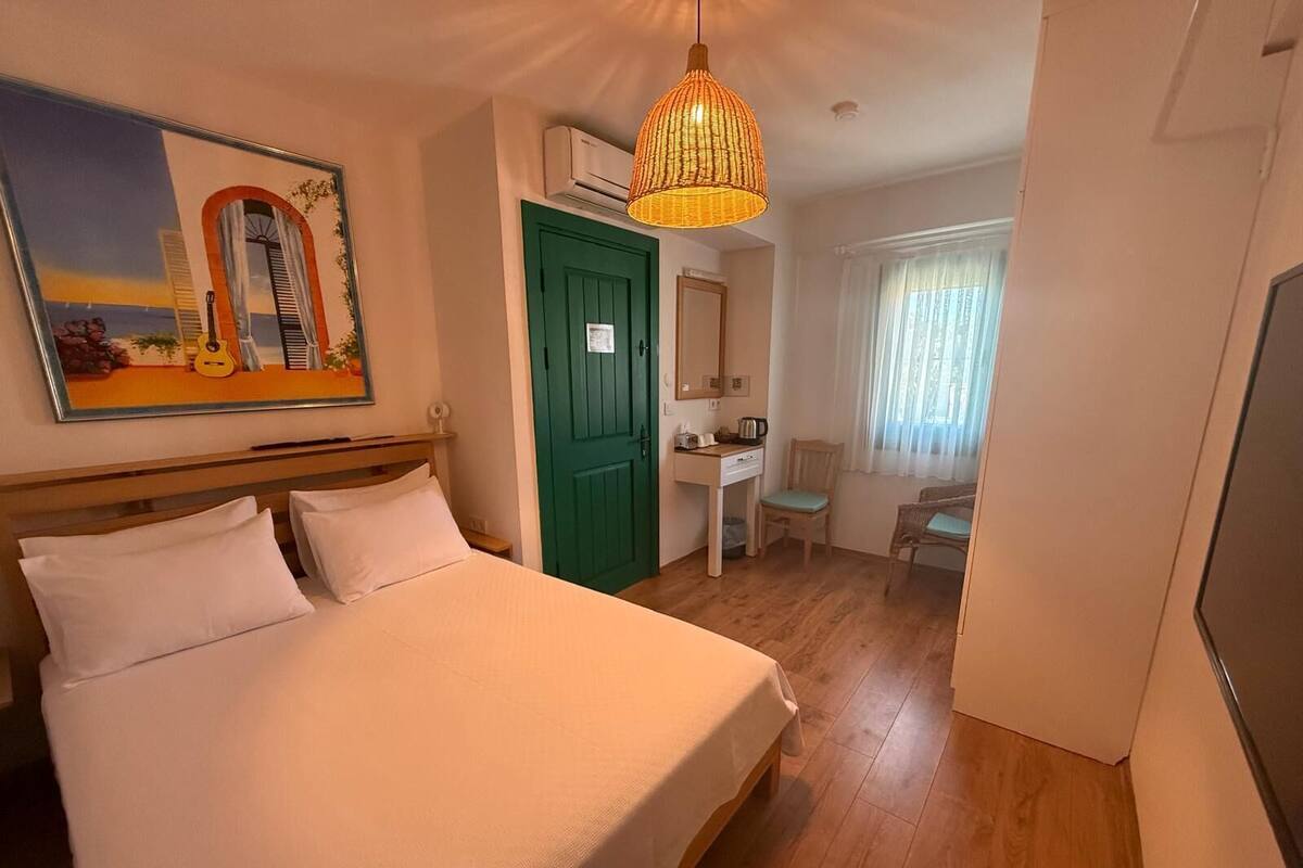 A bedroom with a bed, a desk, a chair, a green door, and a painting on the wall.
