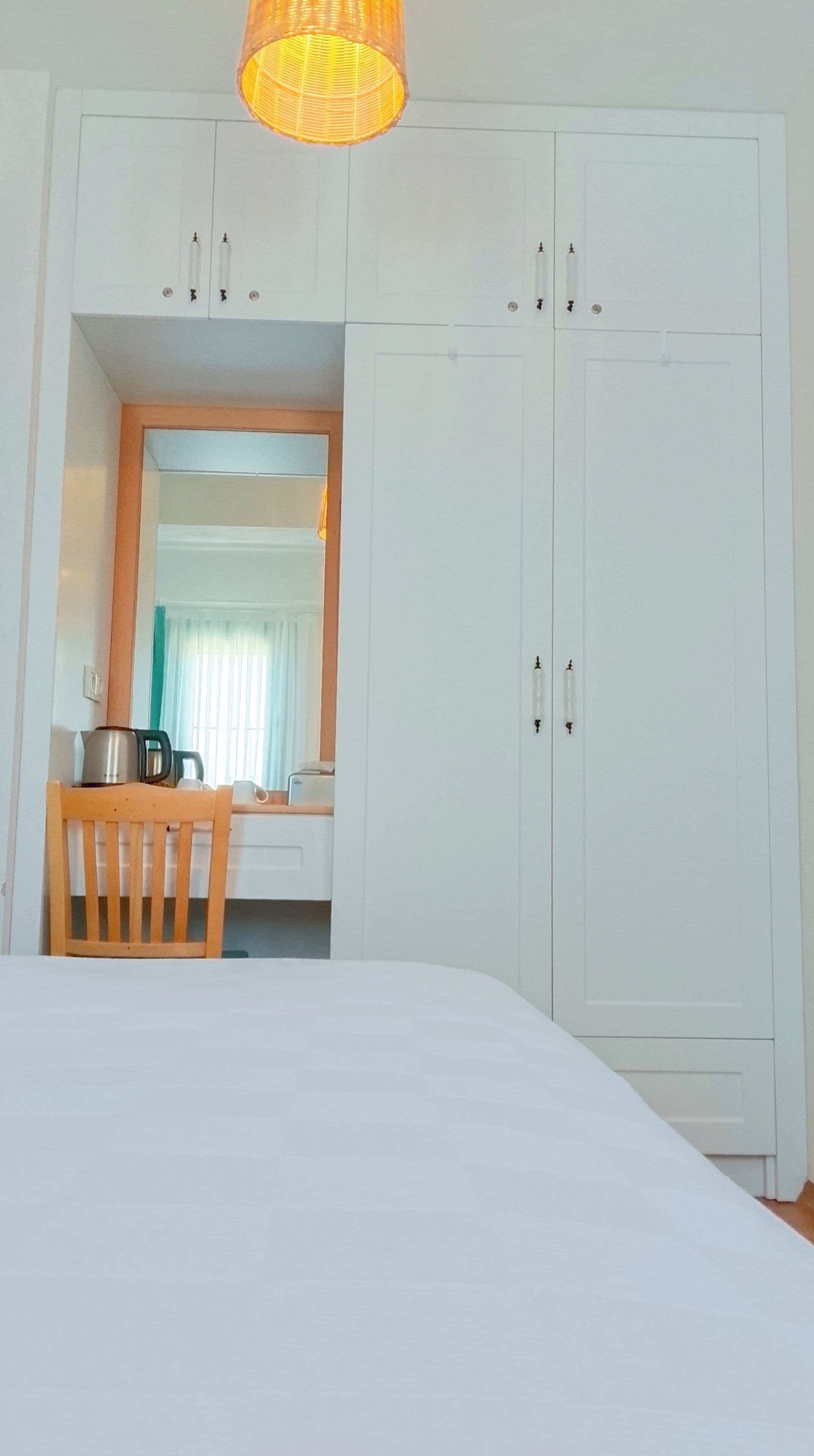 Um quarto com uma cama, uma cadeira de madeira, uma mesa com chaleira e um guarda-roupa.