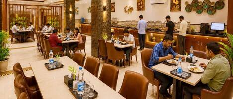 Un espace de restauration d’hôtel comprenant plusieurs tables et chaises, un bar et des œuvres d’art décoratives sur les murs.