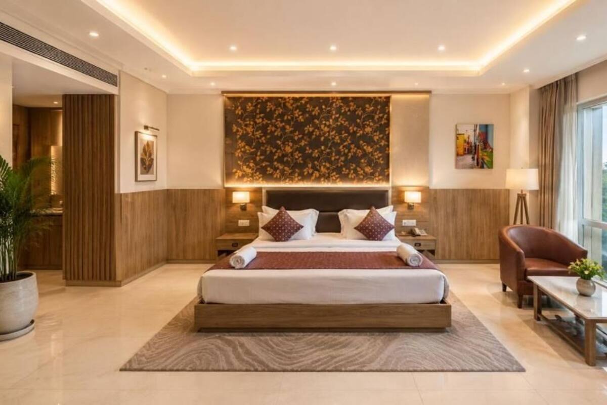 Une chambre d’hôtel moderne, dotée d’un grand lit, de tables de chevet, d’un bureau et offrant une vue sur l’extérieur.