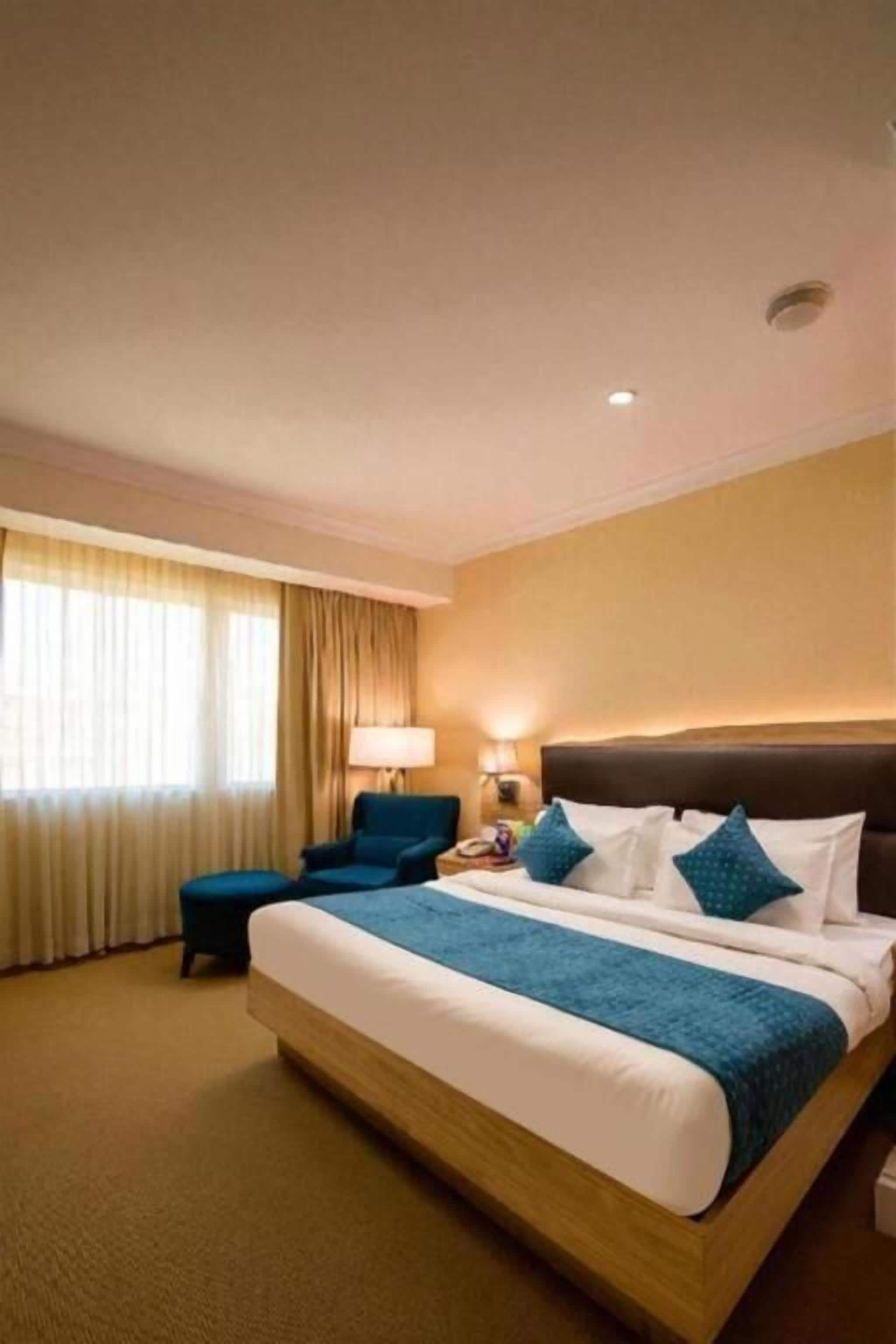 A hotel room with a large bed, a desk, a chair, and a window with curtains.