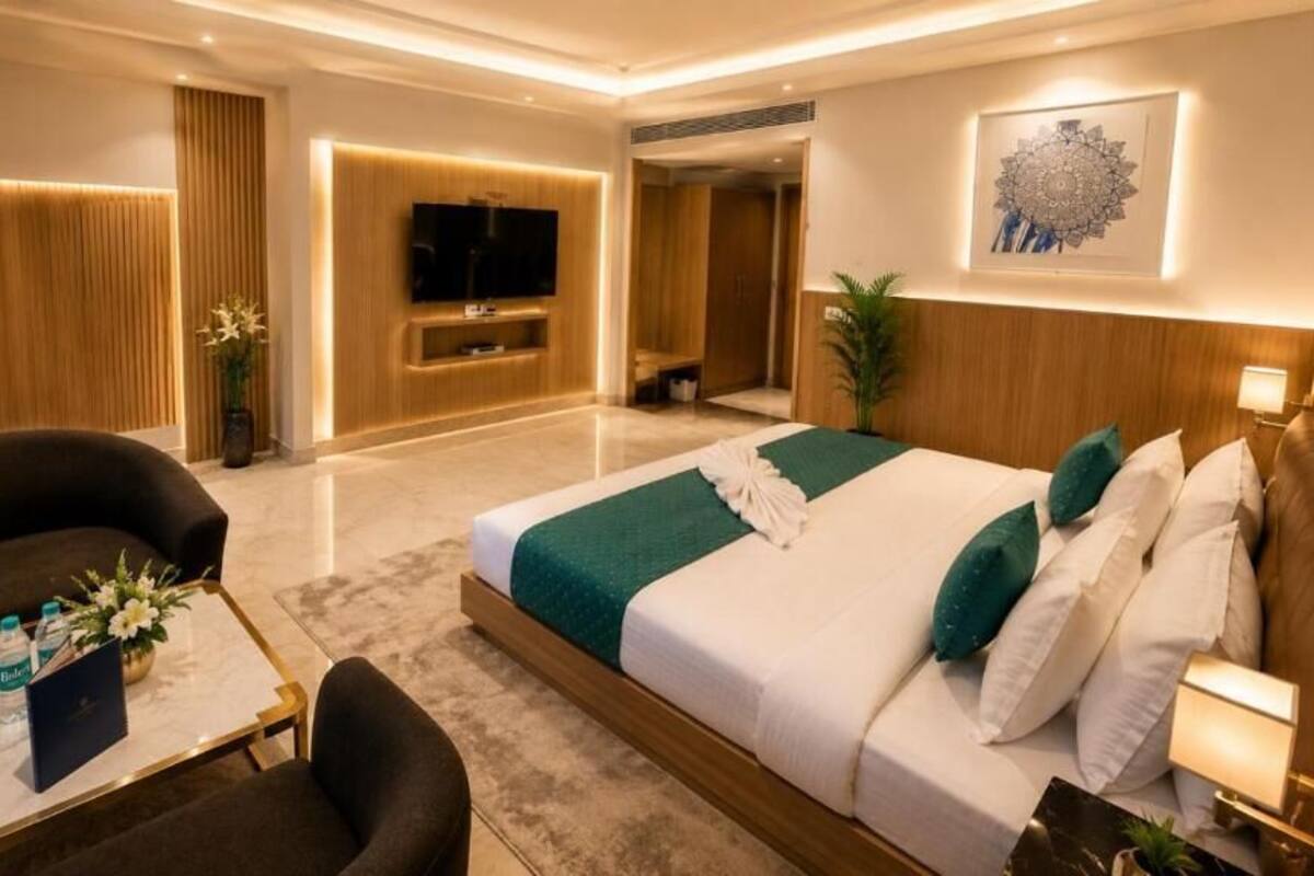 Une chambre d’hôtel moderne dotée d’un grand lit, d’un coin salon avec un canapé et un fauteuil, d’un téléviseur à écran plat et d’une œuvre d’art accrochée au mur.