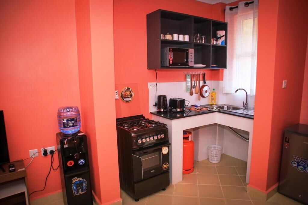 A compact kitchen with a stove, oven, microwave, and a water dispenser.