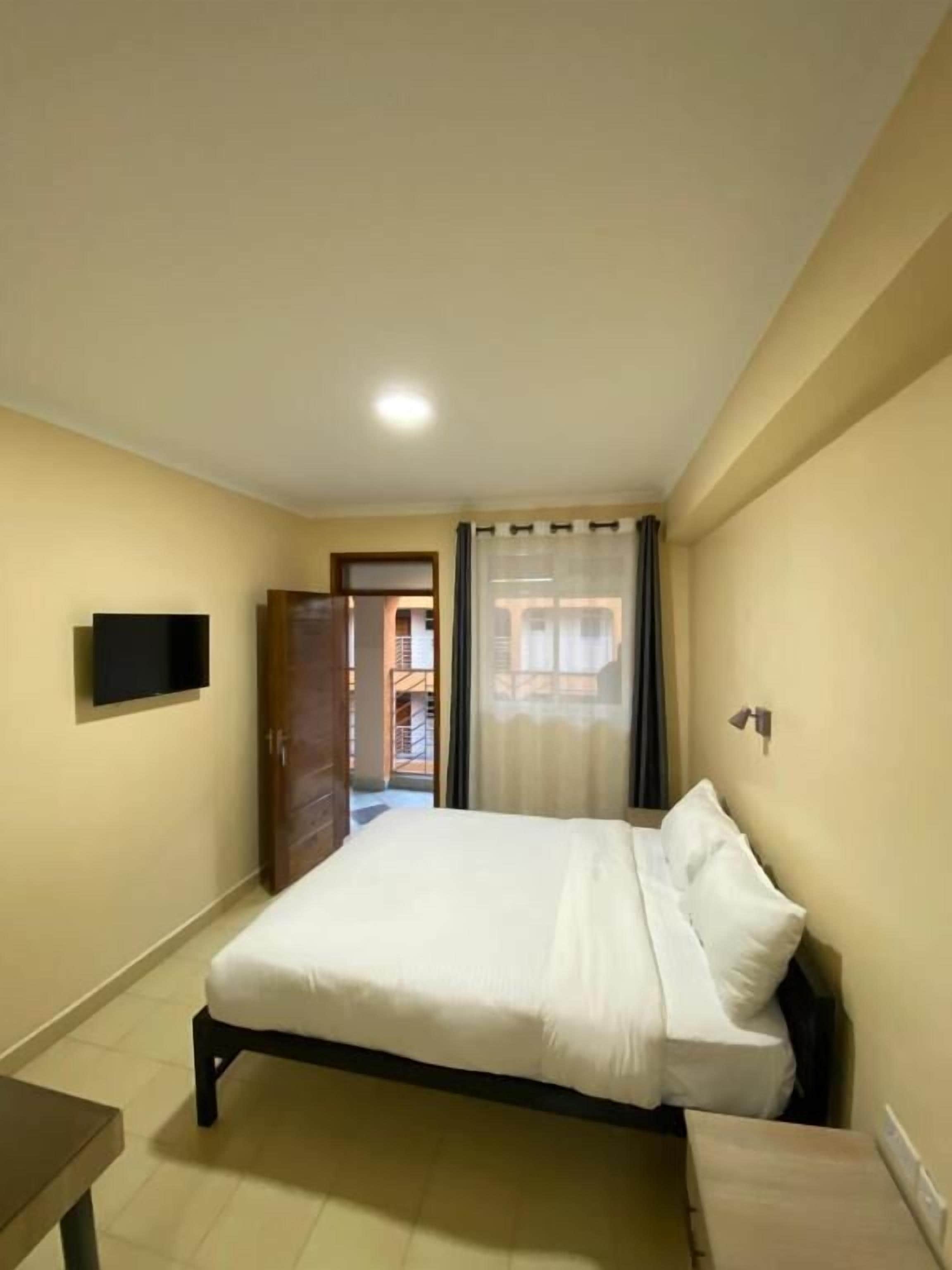 Un dormitorio con cama, televisor, puerta que da a un balcón y una mesita.