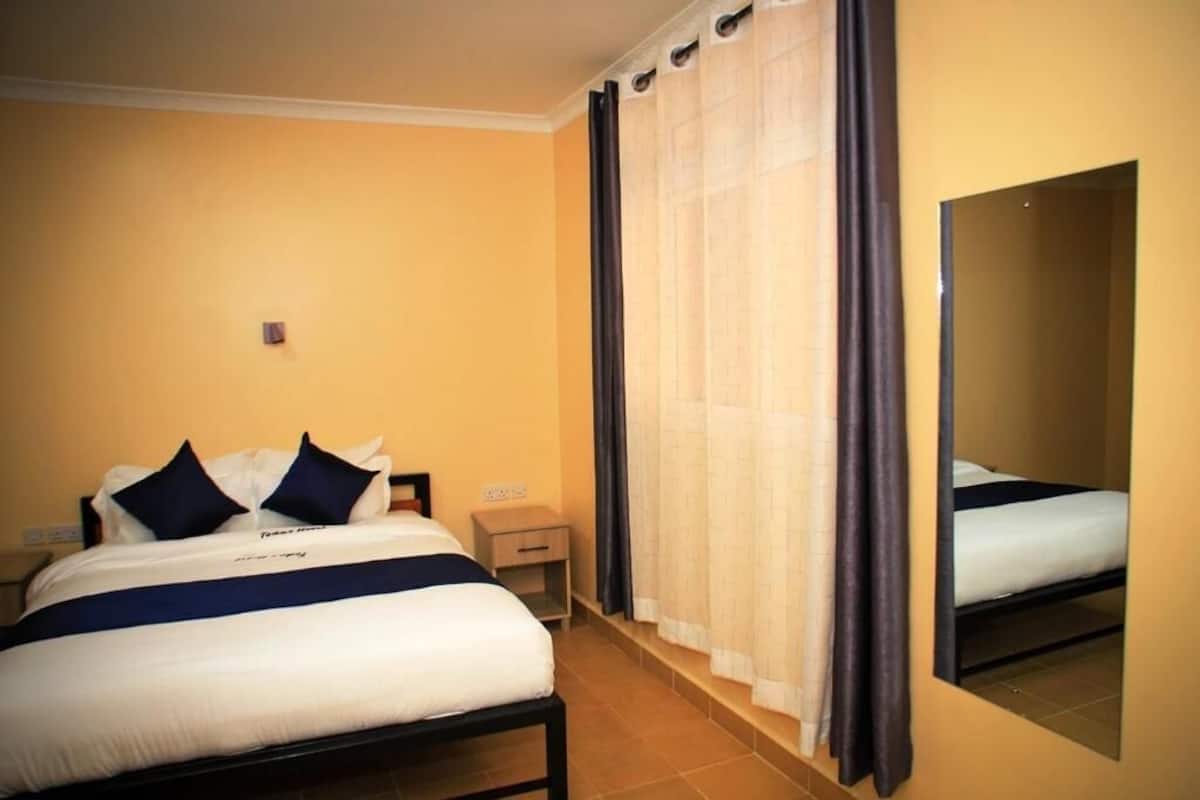 A hotel room with a bed, a nightstand, a mirror, and a window with curtains.