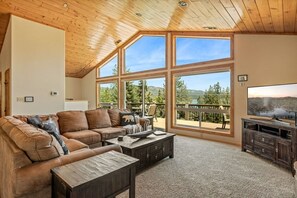 Un salon spacieux avec un grand plafond en bois, un canapé en cuir marron, une table basse et un téléviseur posé sur un meuble en bois.