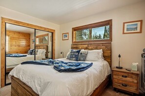 A bedroom with a large bed, a wooden headboard, a window, a mirror, and a nightstand with a lamp. - Snowboard Shores| Game Room | Hot Tub | Lake View (Big Bear Lake)