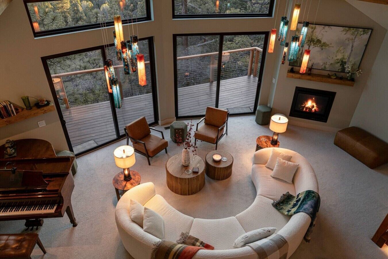 A spacious living room with a piano, comfortable seating, a fireplace, and large windows offering a view of the outdoors.