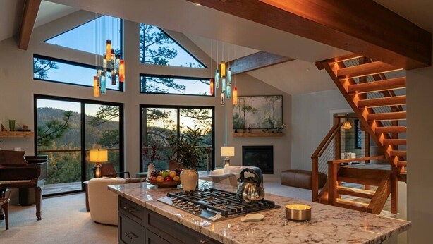 A spacious kitchen with a large island, a piano, and a view of the outdoors through large windows. - Pine & Paw | Hot Tub, Sauna, Games, Views, Piano (Big Bear Lake)