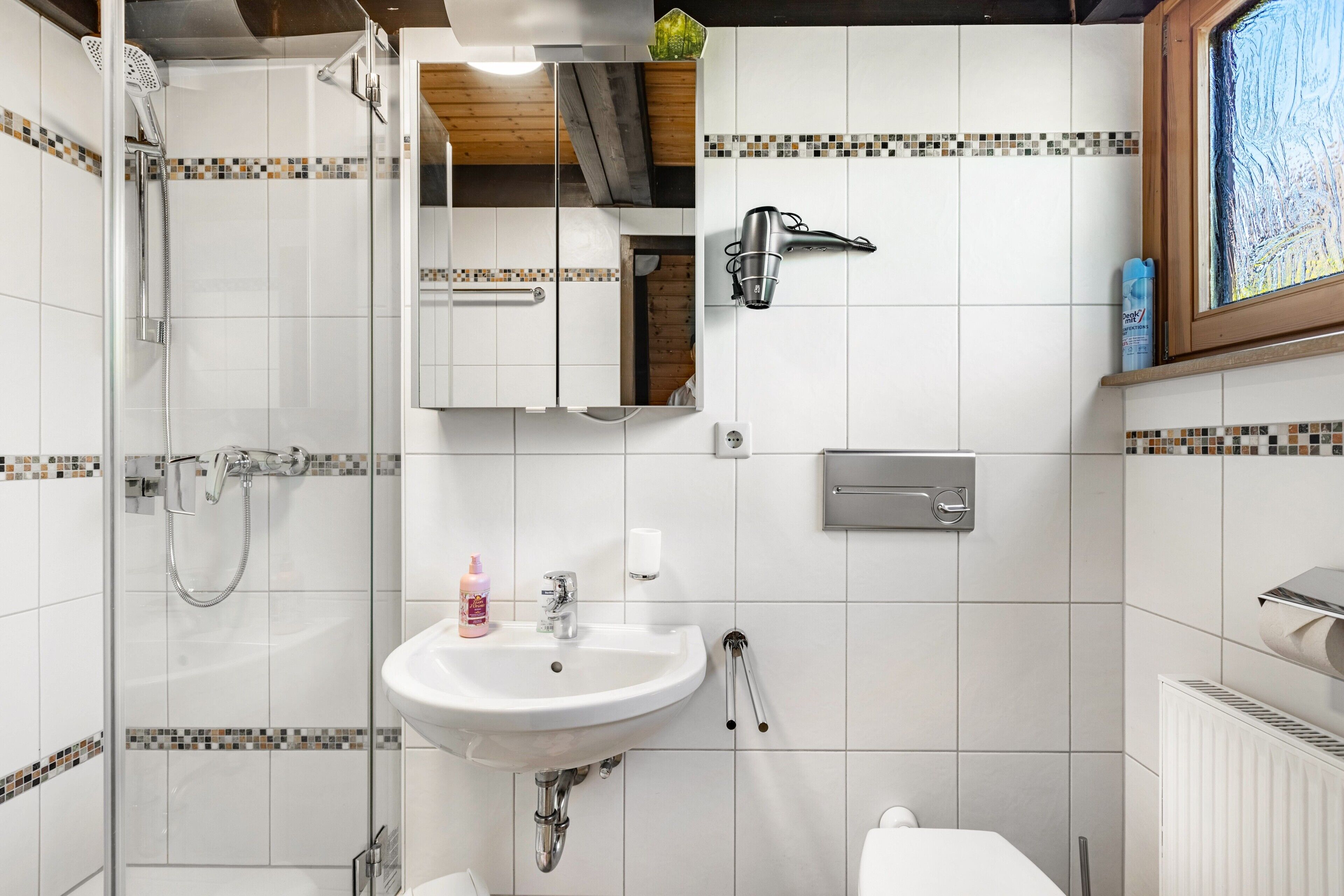 Une salle de bain avec une douche à parois de verre, un lavabo blanc, un miroir et une fenêtre donnant sur un beau paysage.