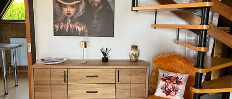 A room with a wooden staircase, a cabinet with drawers, a lamp, and a framed picture on the wall.