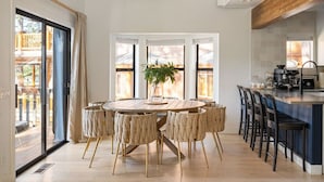 Uma cozinha moderna com ilha central, área de refeições com mesa redonda e cadeiras, e grandes janelas com vista para o exterior.