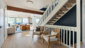 Ampla sala de estar com escada, piso de madeira e vista para o exterior.