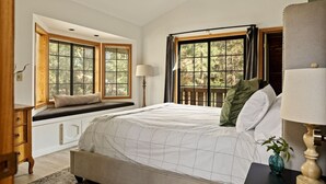 Un dormitorio con una cama grande, un asiento junto a la ventana y vistas a árboles.