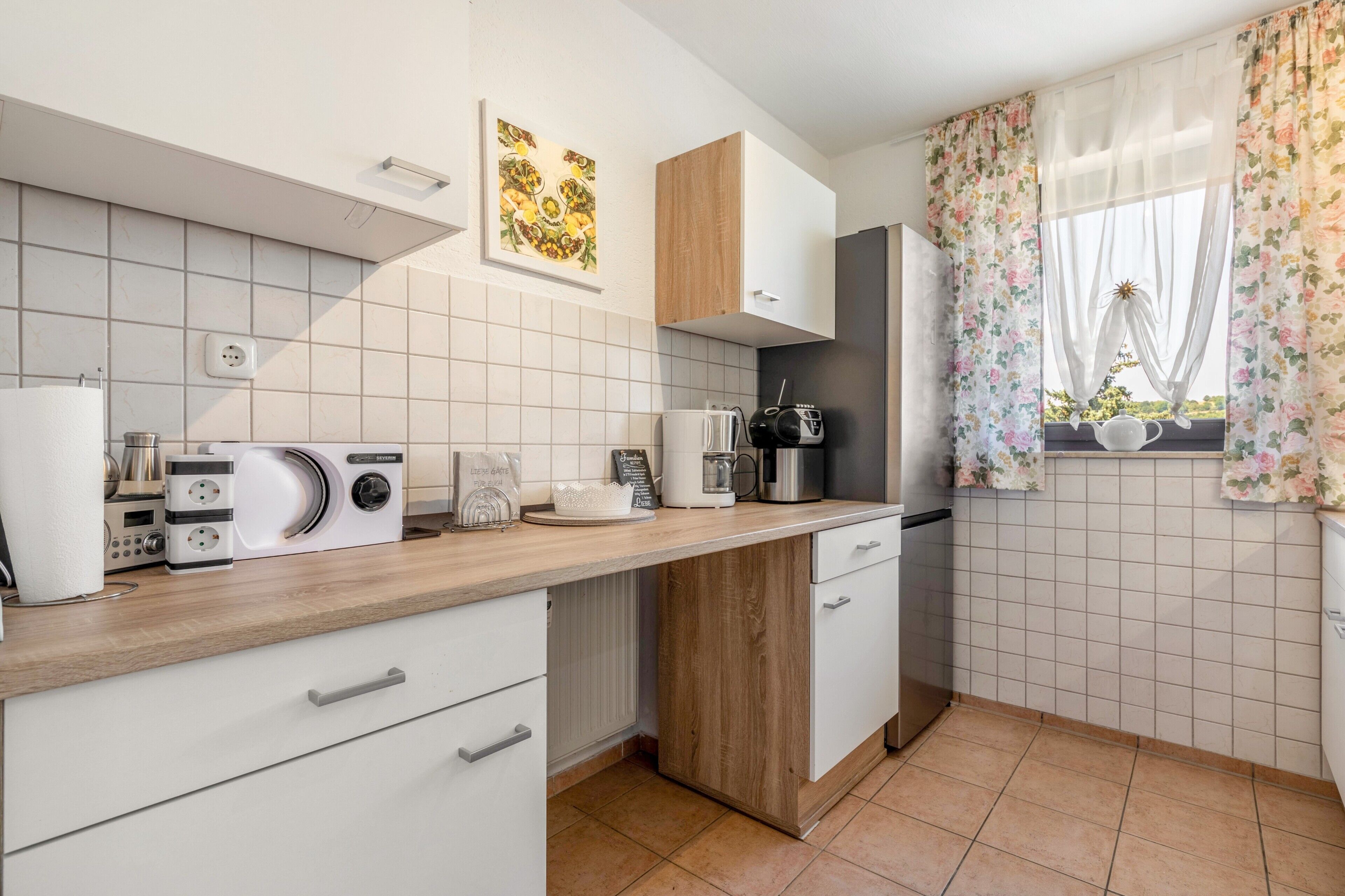 Eine moderne Küche mit weißen Schränken, einer Holz Arbeitsplatte und einem Fenster mit floralen Vorhängen.