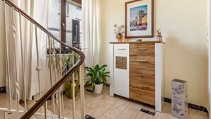 A staircase with a handrail, a potted plant, a wooden cabinet with a framed picture, and a sign on the floor.