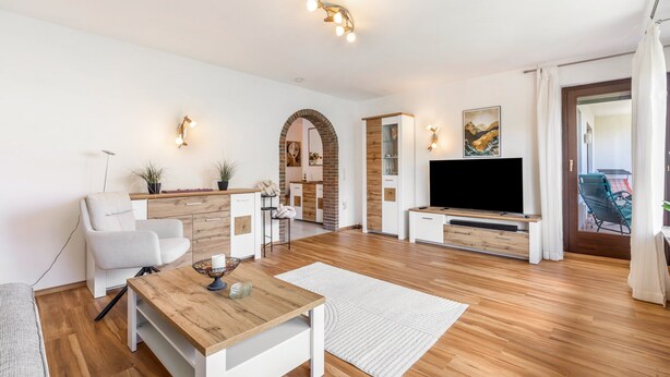 A modern living room with a wooden coffee table, white sofa, TV, and a dining area.