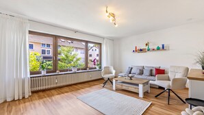 A modern living room with a sofa, coffee table, and chairs, a radiator, and a window with curtains.