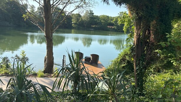 A serene lakeside setting with a wooden dock, surrounded by lush greenery and trees.