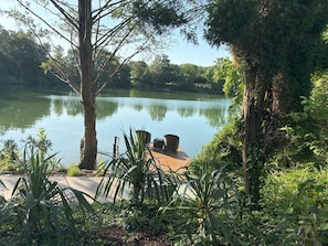 A serene lakeside setting with a wooden dock, surrounded by lush greenery and trees.