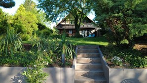 A house with a wooden exterior, a front yard with a lawn, and a concrete staircase leading to the entrance.