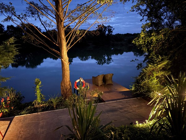 A wooden deck with a lifebuoy, surrounded by lush greenery and a calm lake reflecting the sky.