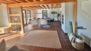 A spacious room with a wooden ceiling, a large rug, and a dining area with a table and chairs.