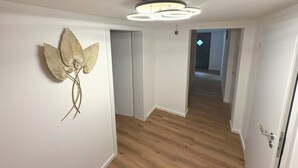 A hallway with wooden flooring, a wall-mounted decorative piece, and a ceiling light fixture.