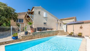 A swimming pool with a stone border, a covered patio with outdoor furniture, and a building with a sloped roof. - Villa 'L'Angloise' with Private Pool, Wi-Fi and Air Conditioning (Les Angles)